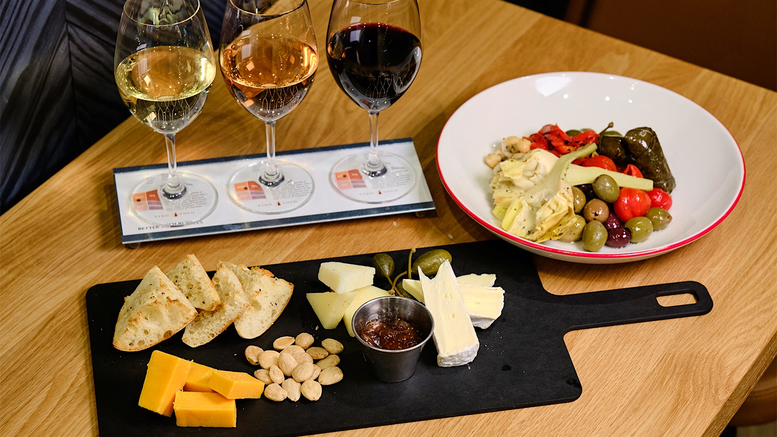 A wine flight including red, white and rosé wine, served along a cheese plate and a bowl of olives at Vino Volo.